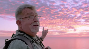 Inogen Customer Len B. gestures toward a sunrise over the ocean while using his Inogen One oxygen concentrator