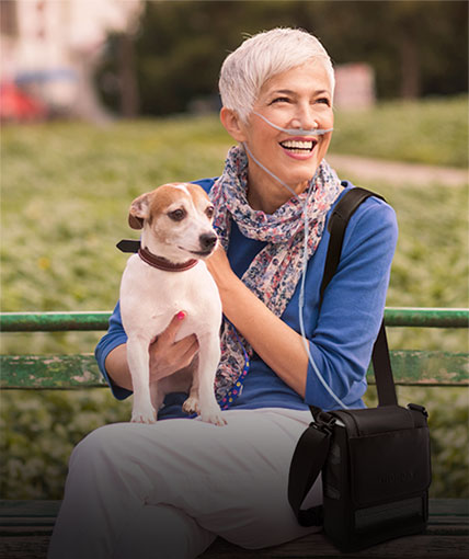 Woman and dog on a park bench with an Inogen Portable Oxygen Concentrator