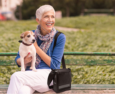 Woman and dog on a park bench with an Inogen Portable Oxygen Concentrator