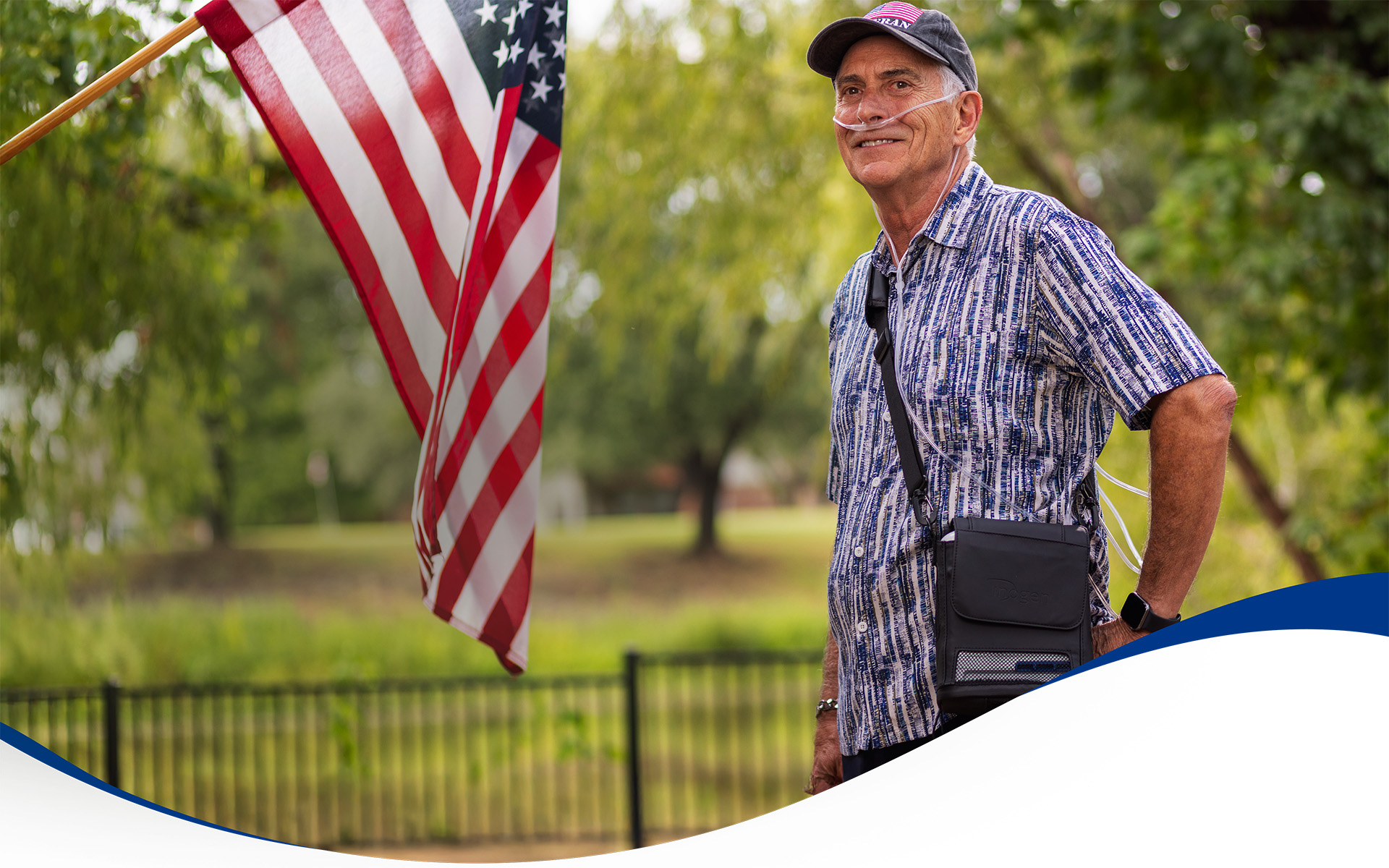 A proud veteran using an Inogen portable oxygen concentrator standing in his yard next to an American flag