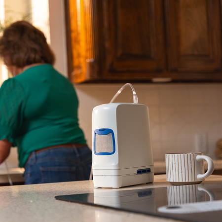 An Inogen Rove 4 portable oxygen concentrator next to a coffee cup on a kitchen counter